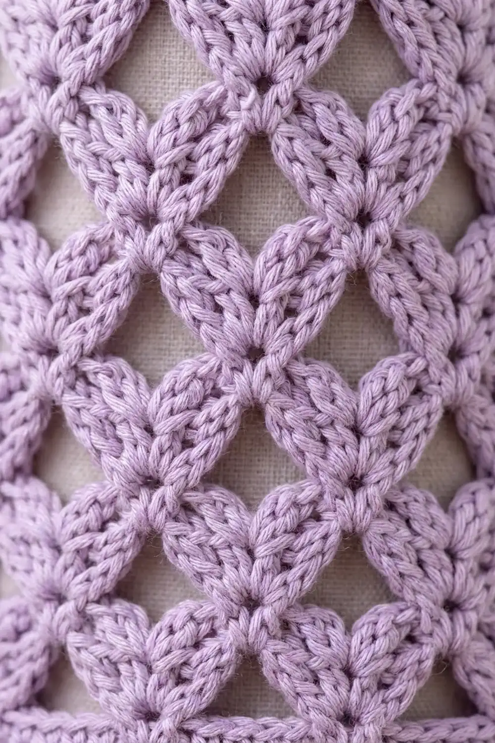 Lavender crocheted fabric displaying an openwork heart motif pattern against a light neutral background.