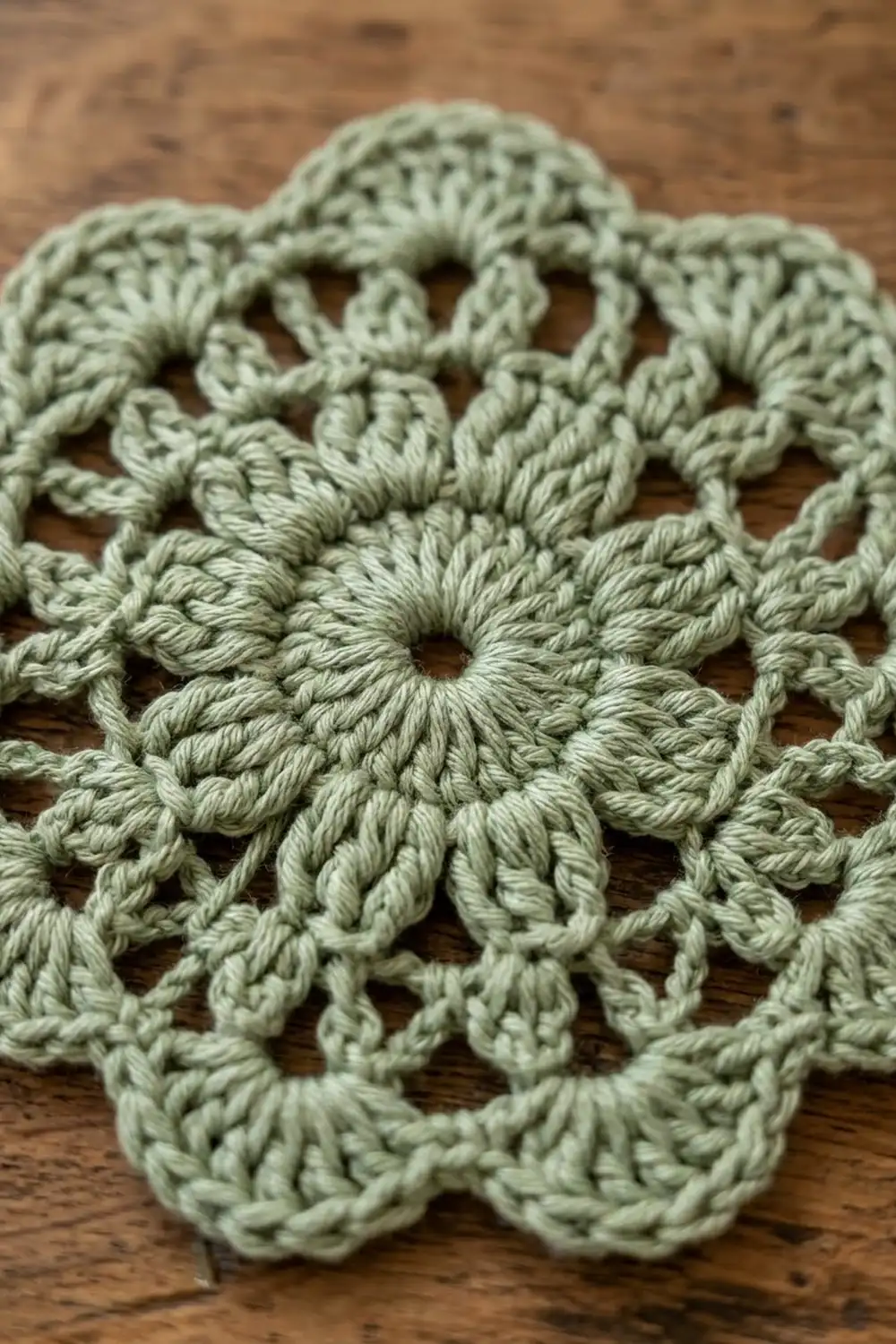 Delicate sage-green crocheted lace with intricate flower motifs resting on a natural wooden surface.