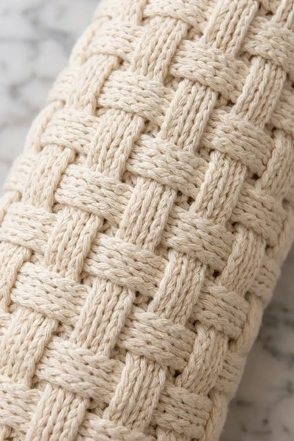 Cream-colored crocheted fabric with interwoven strands creating a detailed basket-weave pattern.