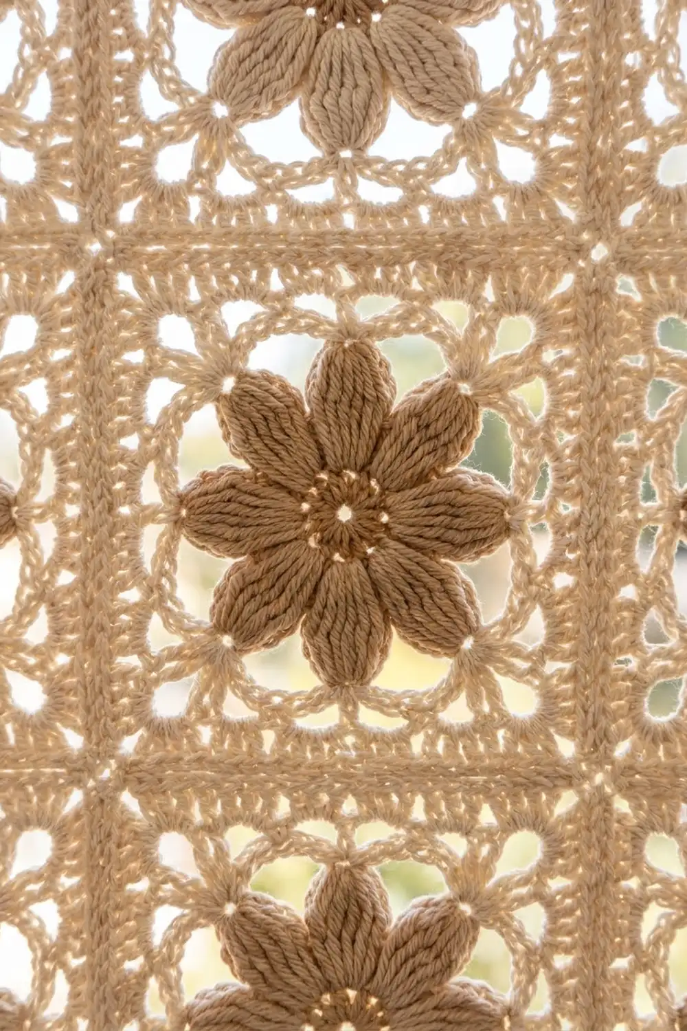 Beige rope lace featuring central six-petaled flower motif, open geometric grid, revealing sky and greenery beyond.