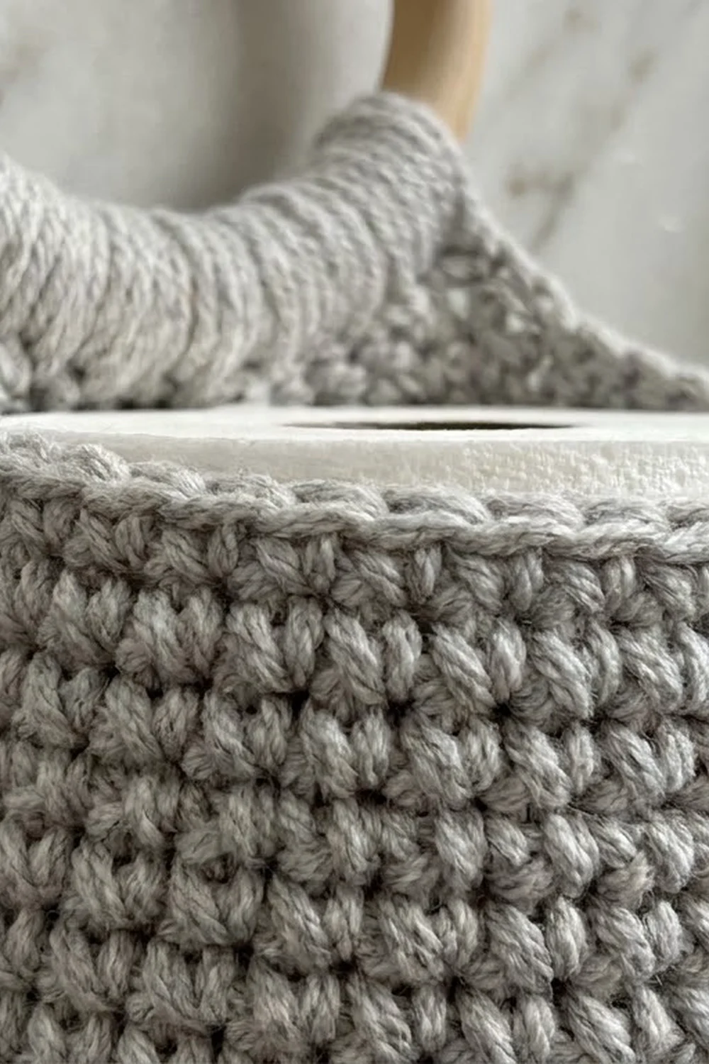 Close-up of cream-colored crocheted fabric showing detailed textured stitches with a wooden needle.