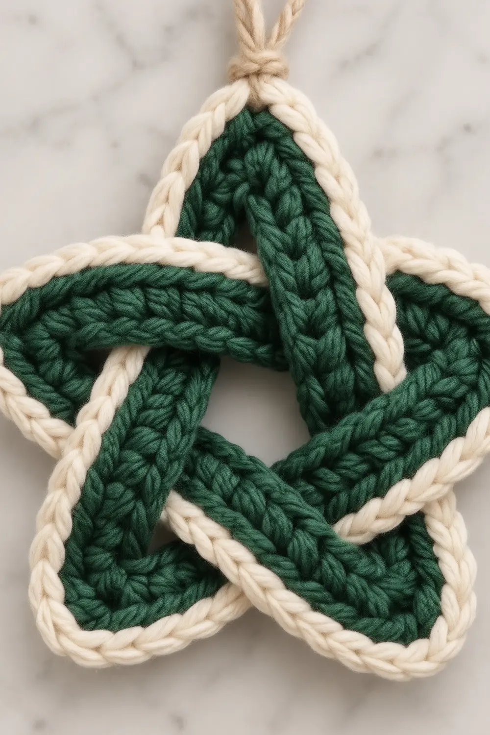 A handmade five-pointed star ornament crafted from braided green and cream-colored yarn with a jute string loop.