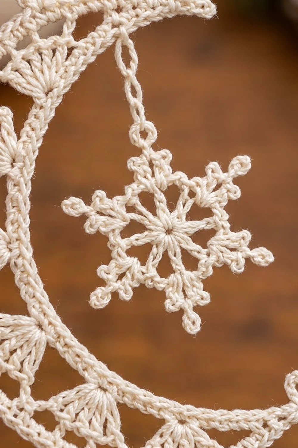 Delicate cream crocheted snowflake with lace details suspended against a warm, softly blurred brown background.