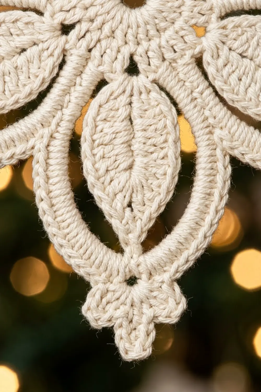 Close-up of cream-colored macramé leaf ornament with intricate braided texture against warm golden bokeh background.