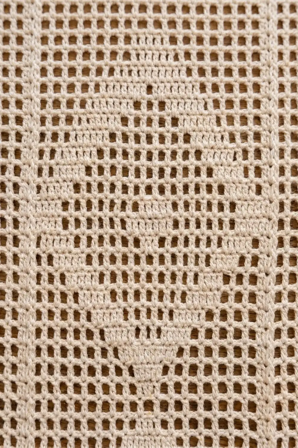 Close-up of cream-colored crocheted lace with uniform square openwork pattern throughout fabric.