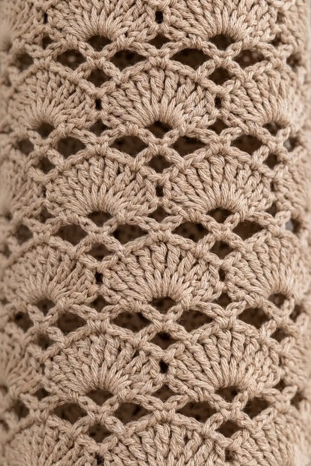 Close-up of natural beige crochet with an open diamond-pattern weave showing detailed yarn texture and shadows.