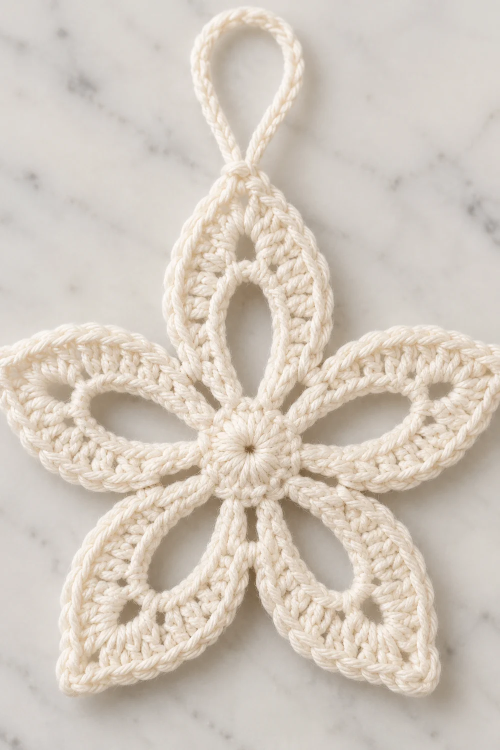 A cream-colored crocheted star ornament with five pointed petals and a loop hanging attachment on marble.