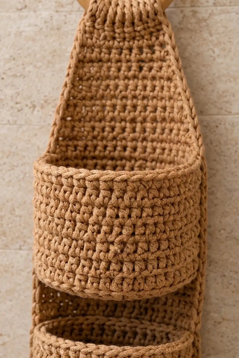 Tan crocheted jute basket with openwork panels and textured center band, photographed against a light stone surface.