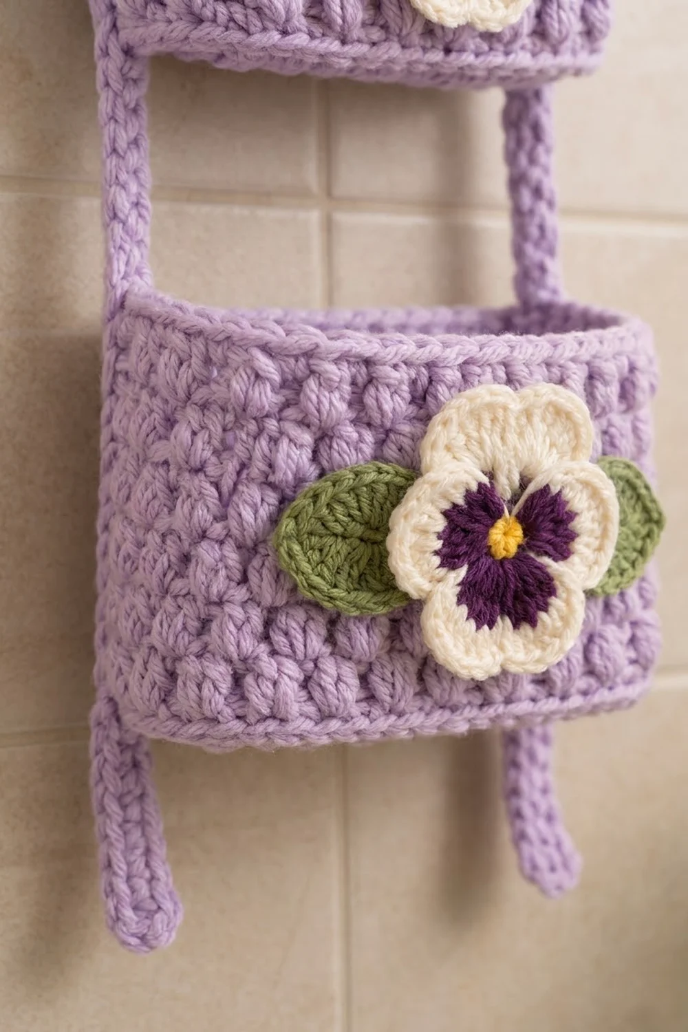 A crocheted lavender basket with cream, purple, and yellow pansy flower on a tiled background.