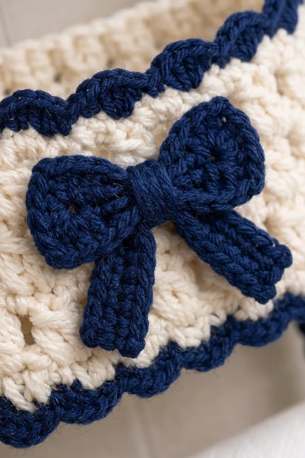 Navy blue crocheted trim with bobble details adorning cream-colored crochet fabric, showing textured stitch work.