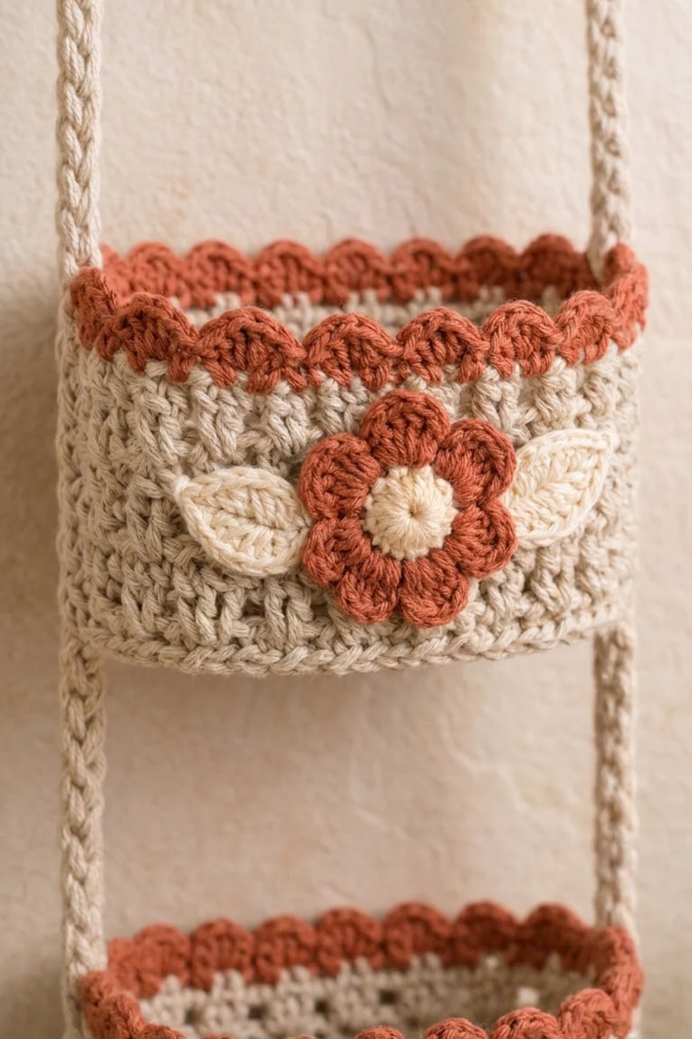Crocheted cream basket with rust-toned scalloped trim edges and a small flower appliqué detail on the side.