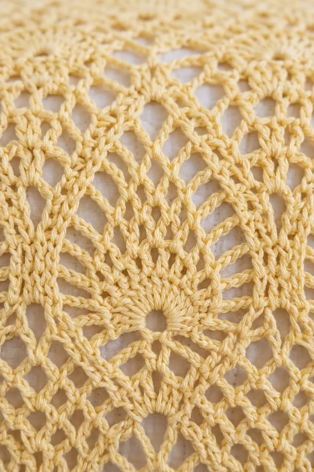 Close-up of cream-colored crocheted lace with intricate diamond-shaped openings and textured rope stitching on white background.