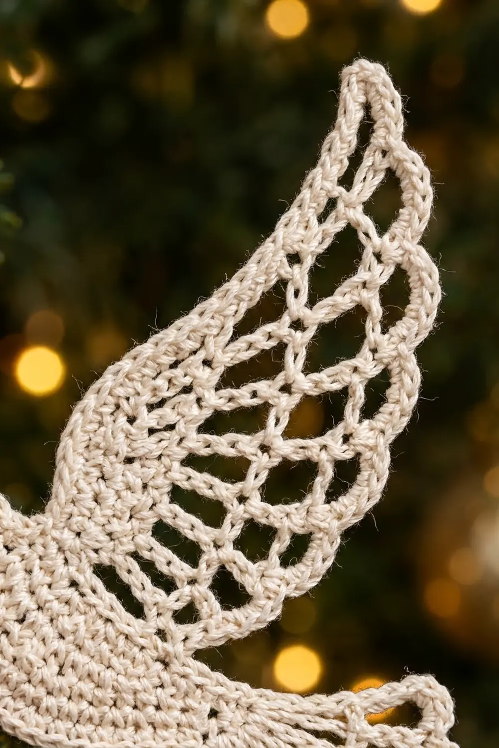 Cream-colored crocheted lace with open lattice pattern and texture against blurred golden bokeh background.