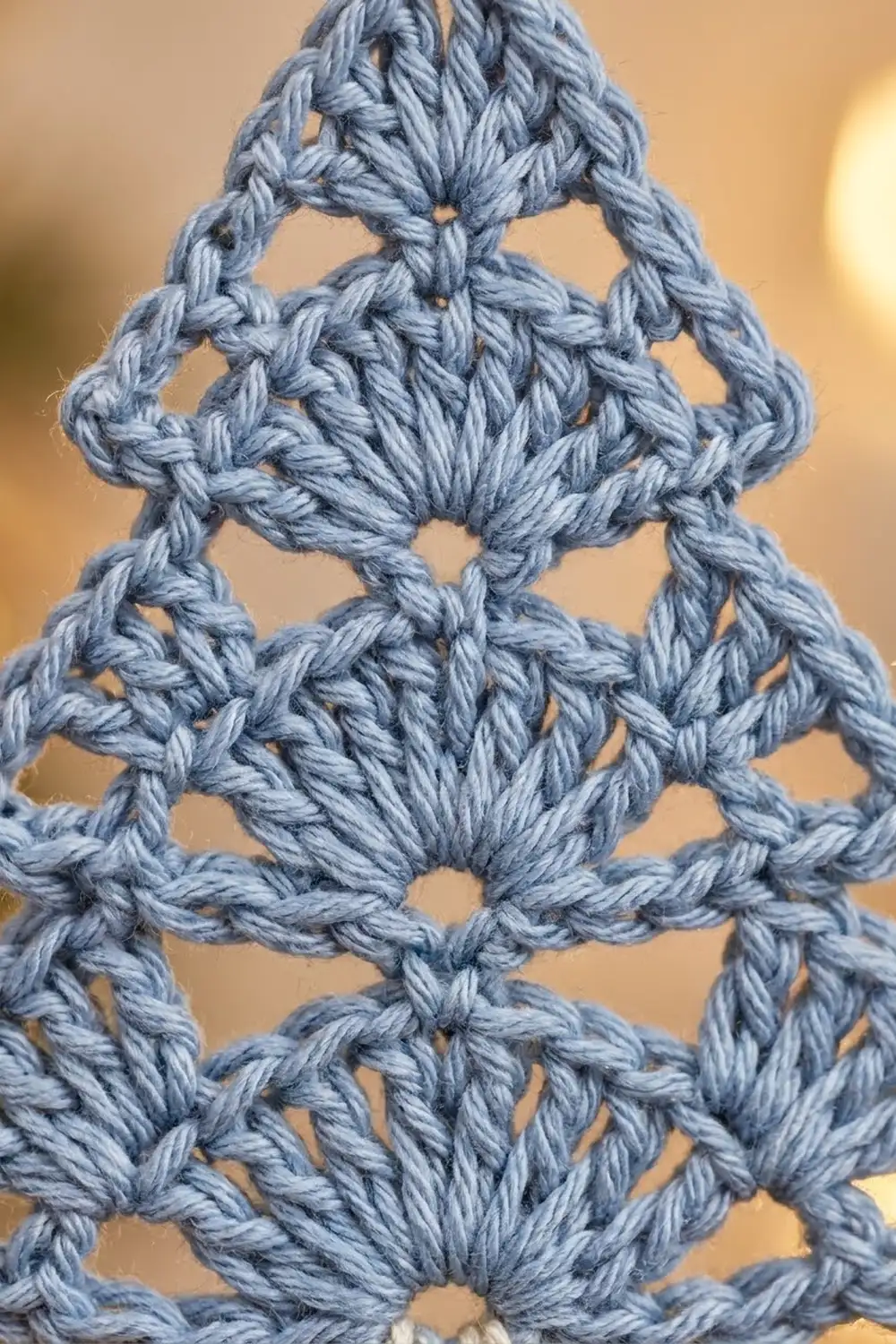 Intricate blue-gray crochet lace with diamond-shaped openwork creates a delicate geometric pattern against a warm, soft background.