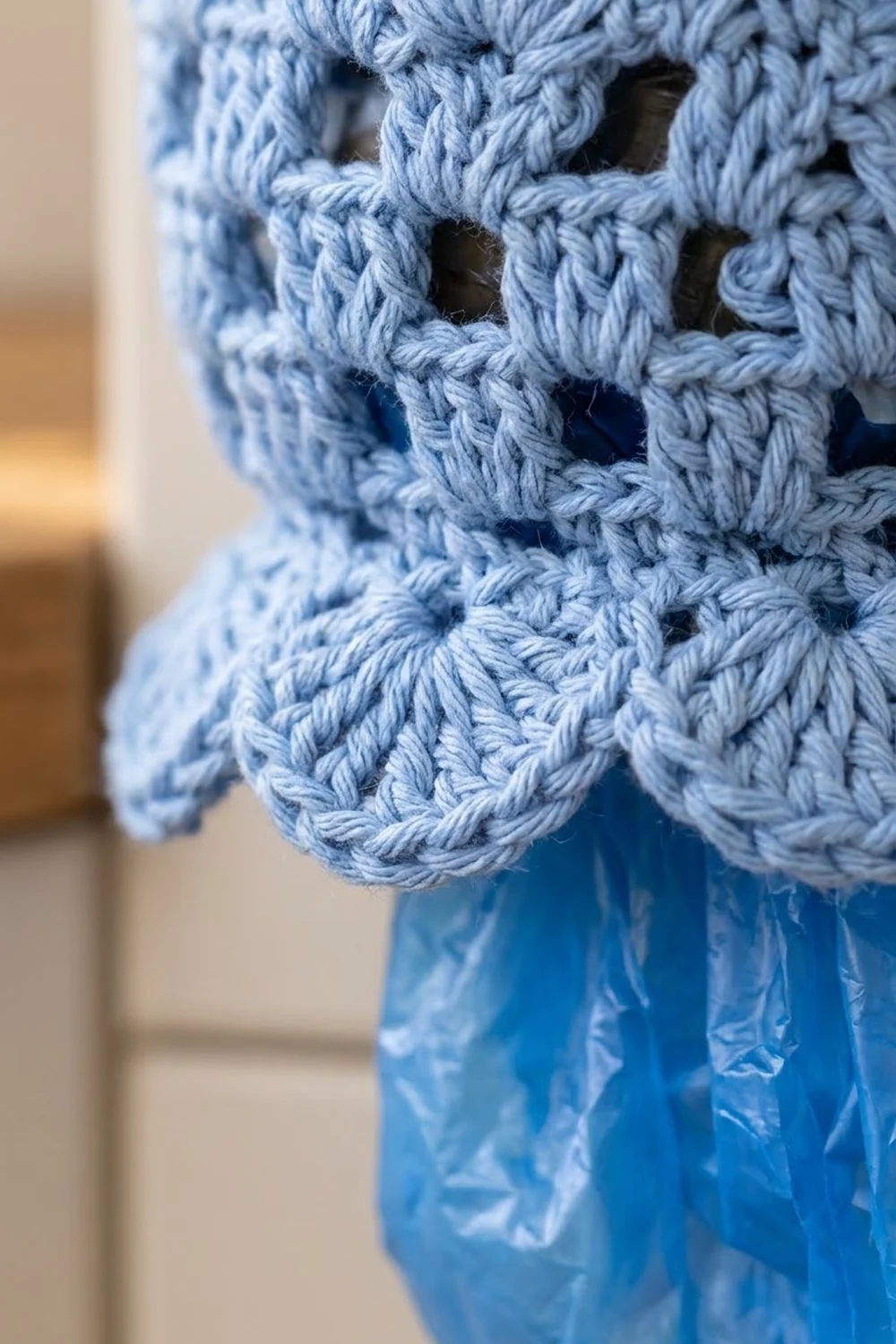 Close-up of light blue crocheted openwork fabric with square holes, showing detailed stitch texture against a blurred background.