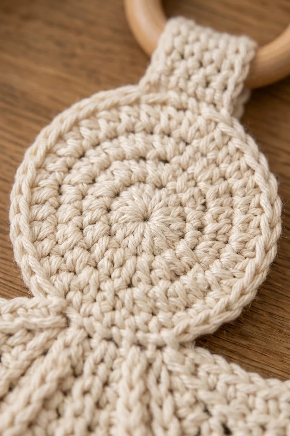 Cream-colored crocheted item with detailed bumpy texture displayed by hands above warm wooden surface.