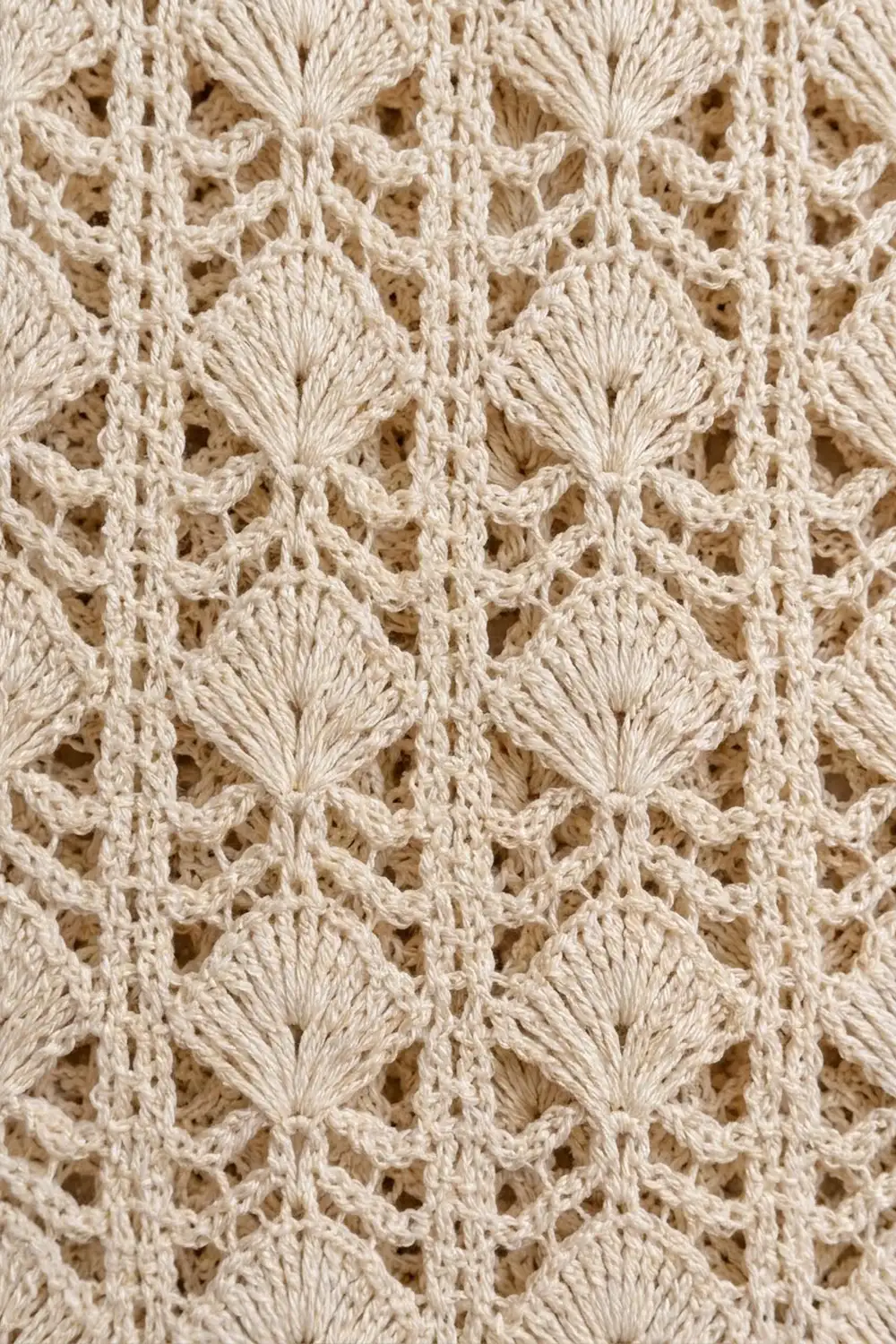 Close-up of cream crochet lace featuring repeating shell stitches with openwork details and delicate texture.
