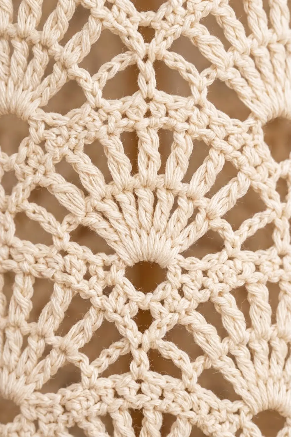 Cream-colored crocheted mesh with geometric twisted-cord lattice pattern against a soft neutral blurred background.