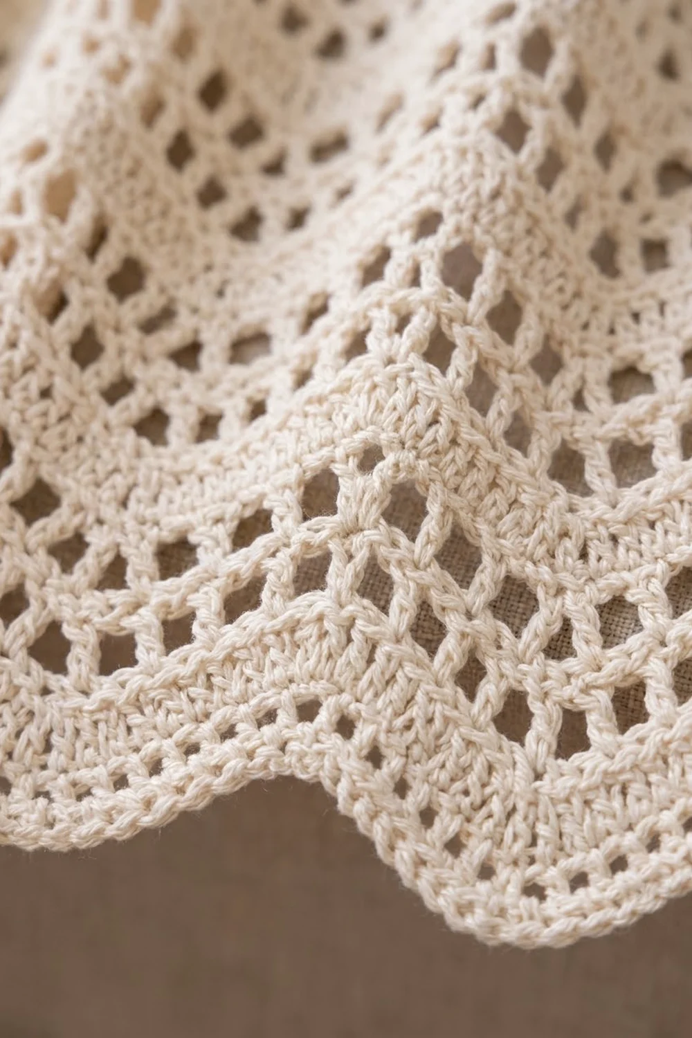Closeup detail of cream crochet lace with repeating diamond-shaped holes, layered to showcase the intricate stitch work.