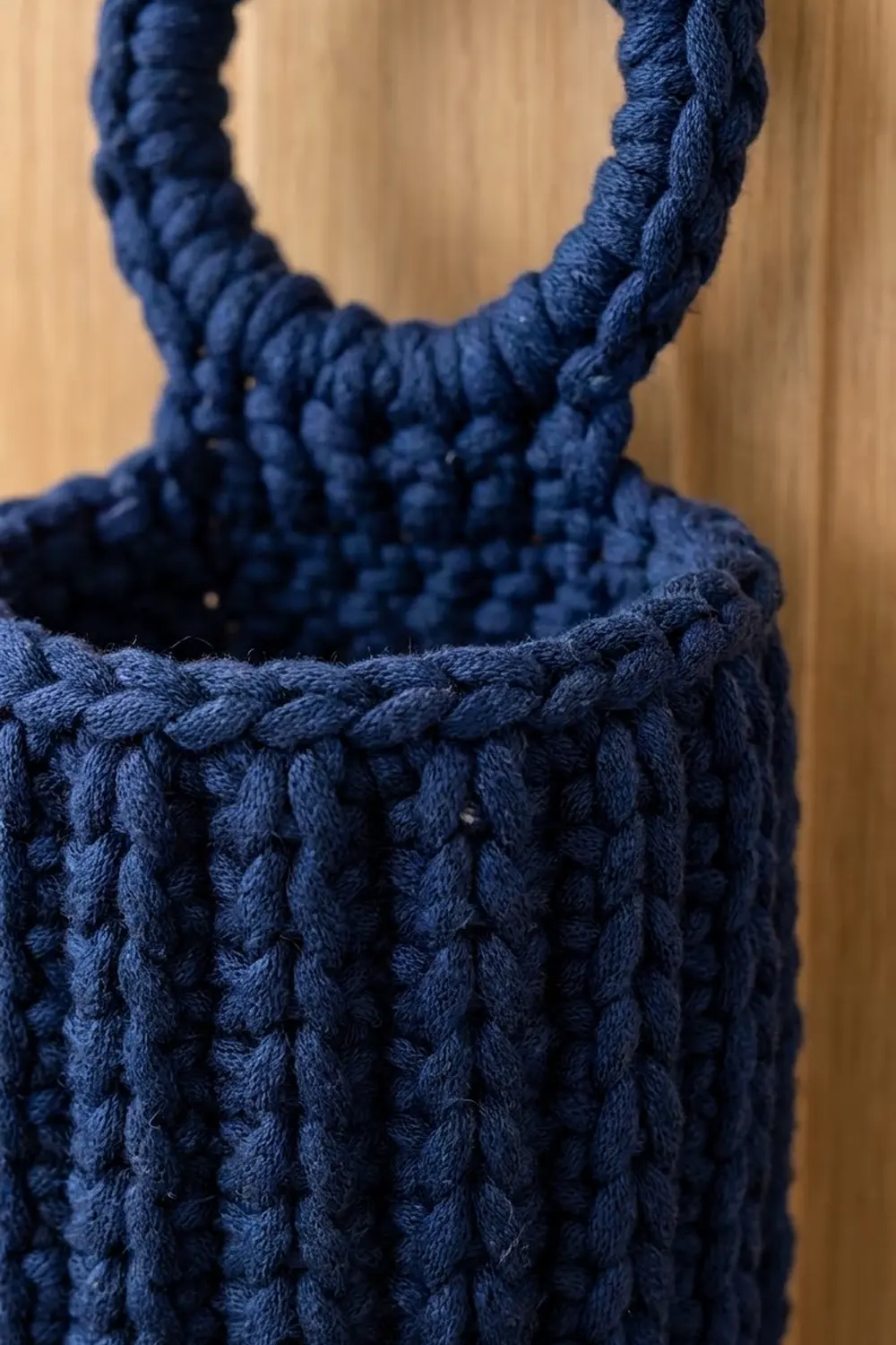 Navy crocheted bag with textured stitches and thick twisted rope handles against a soft beige background.
