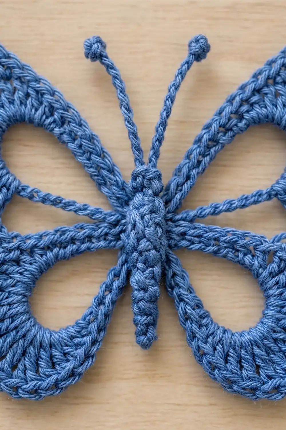 A close-up of a blue crocheted butterfly ornament with knotted antennae, showing detailed rope stitching on a light wood surface.