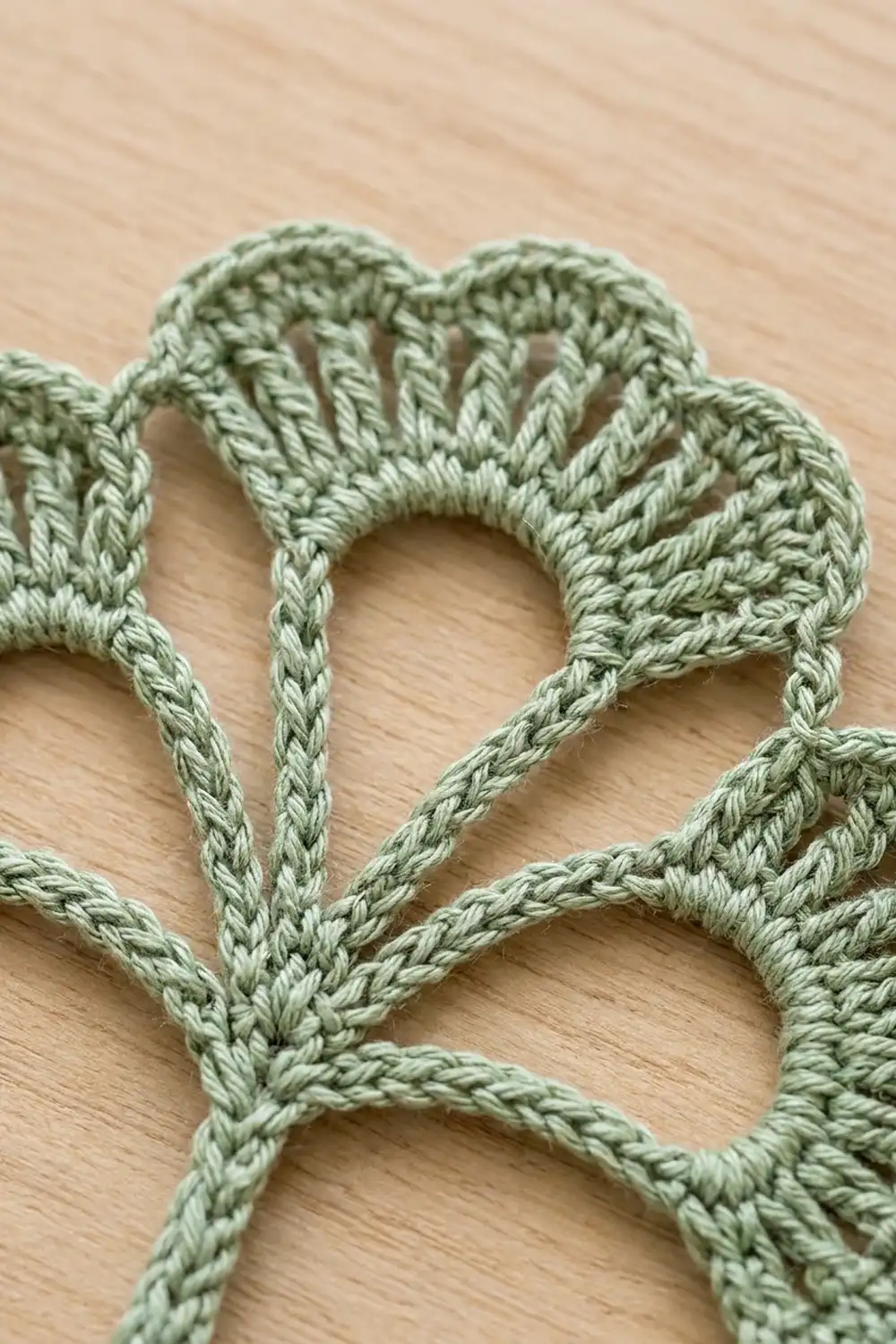Close-up of sage green crochet with loopy stitch texture on light wooden background.
