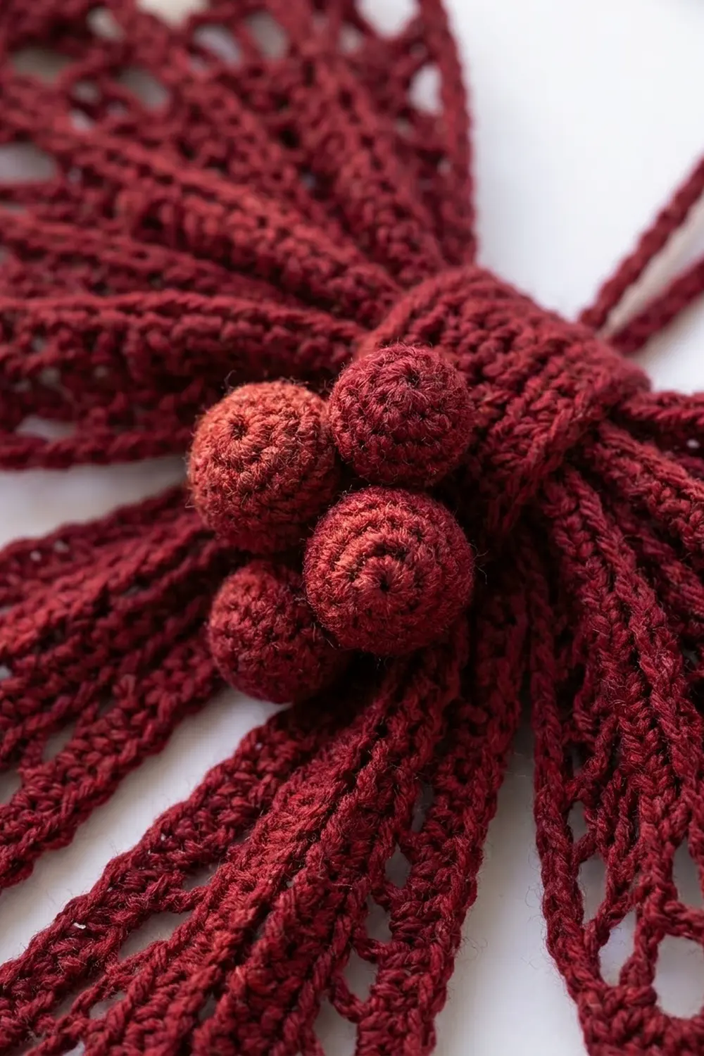 Burgundy crocheted lace with three peachy-rose pompoms adorning the openwork fringe strands.