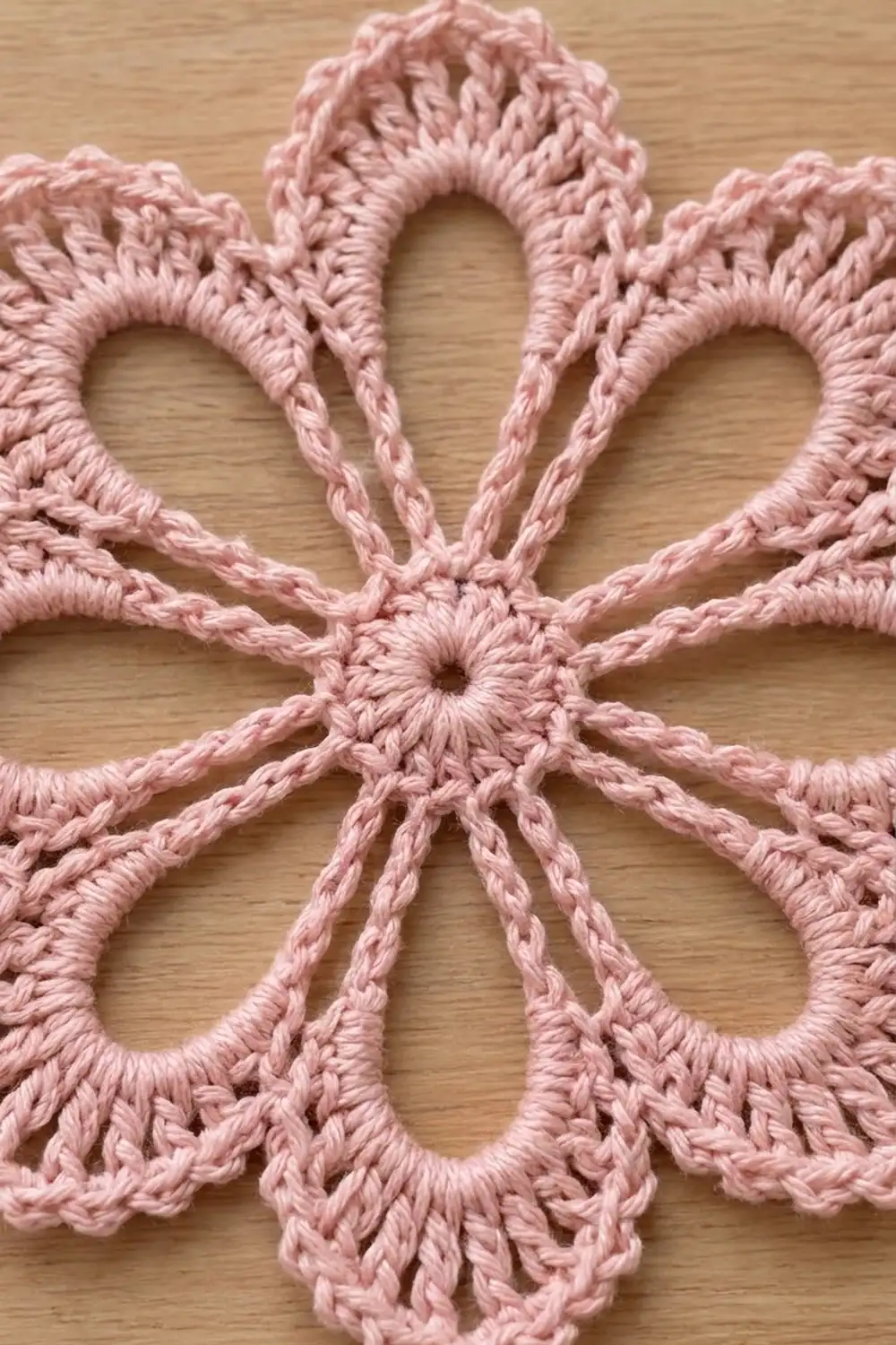 Close-up detail of pink crocheted lace motif with symmetrical teardrop-shaped holes on light wood.