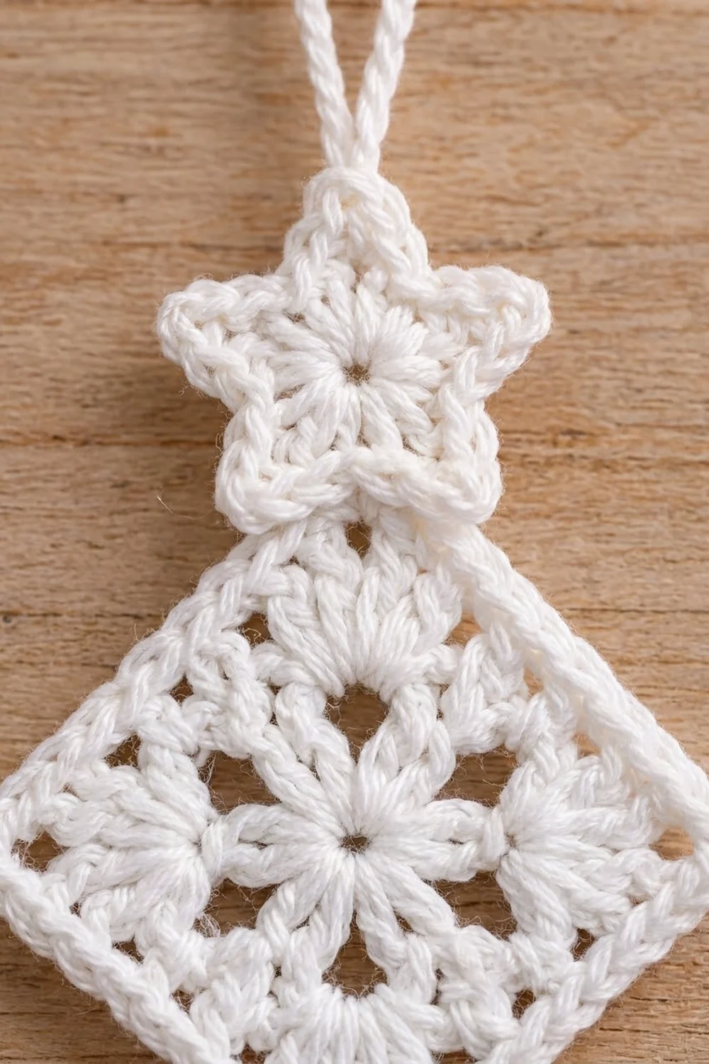 Delicate white crochet snowflake ornament with openwork lace pattern hanging against wooden surface.