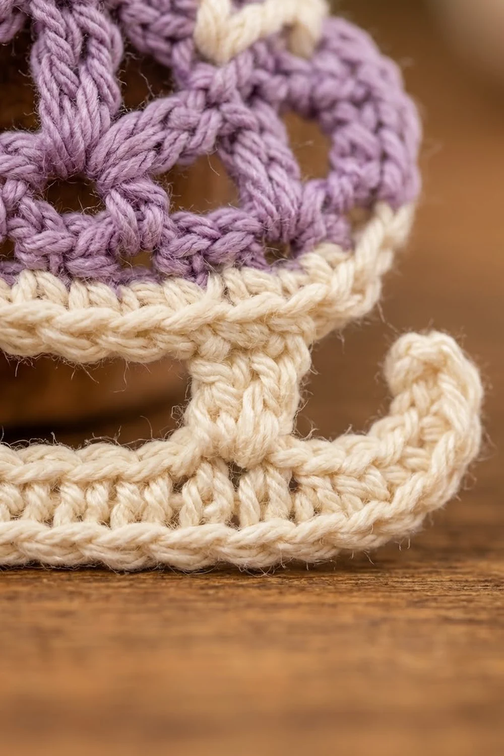 Close-up of crocheted rope stitches in purple and cream yarn on a wooden surface.