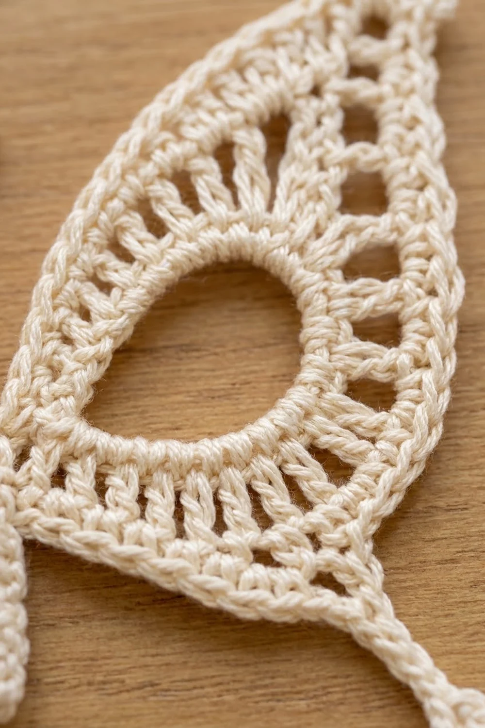Close-up of cream-colored crochet lace with geometric openings and textured stitches on warm wood background.