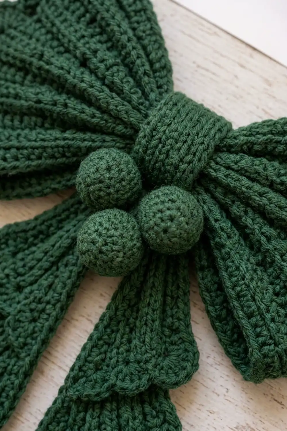 Forest green crocheted fabric with decorative bobbles tied with matching cord on light wood.