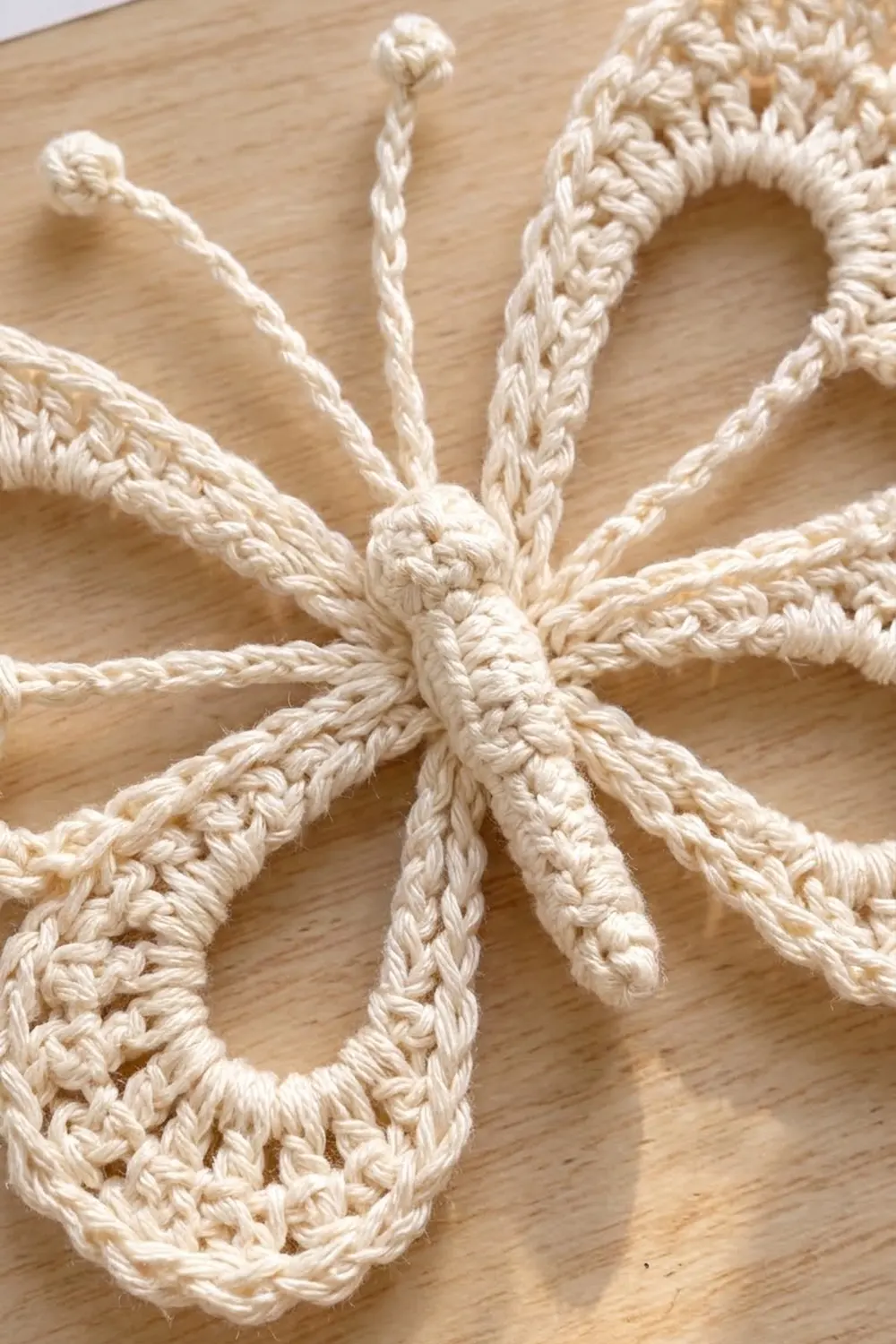 Cream-colored crochet with detailed stitching and knotted centers displayed on a light wooden surface.