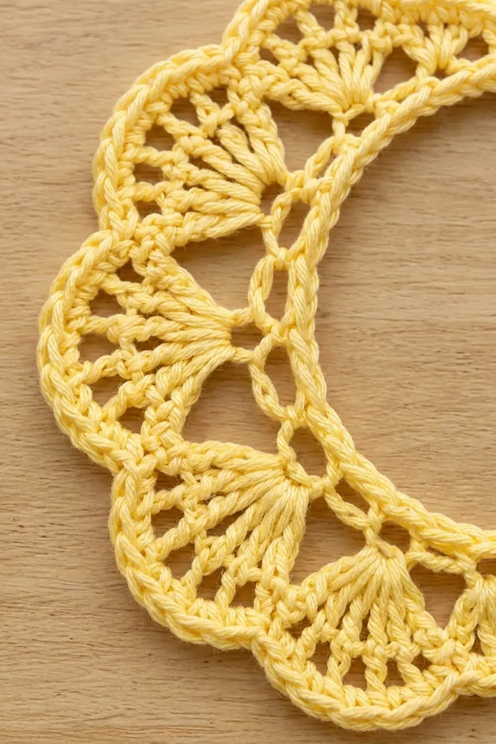Golden-yellow crochet lace with geometric openwork stitches displayed on a light wooden surface.