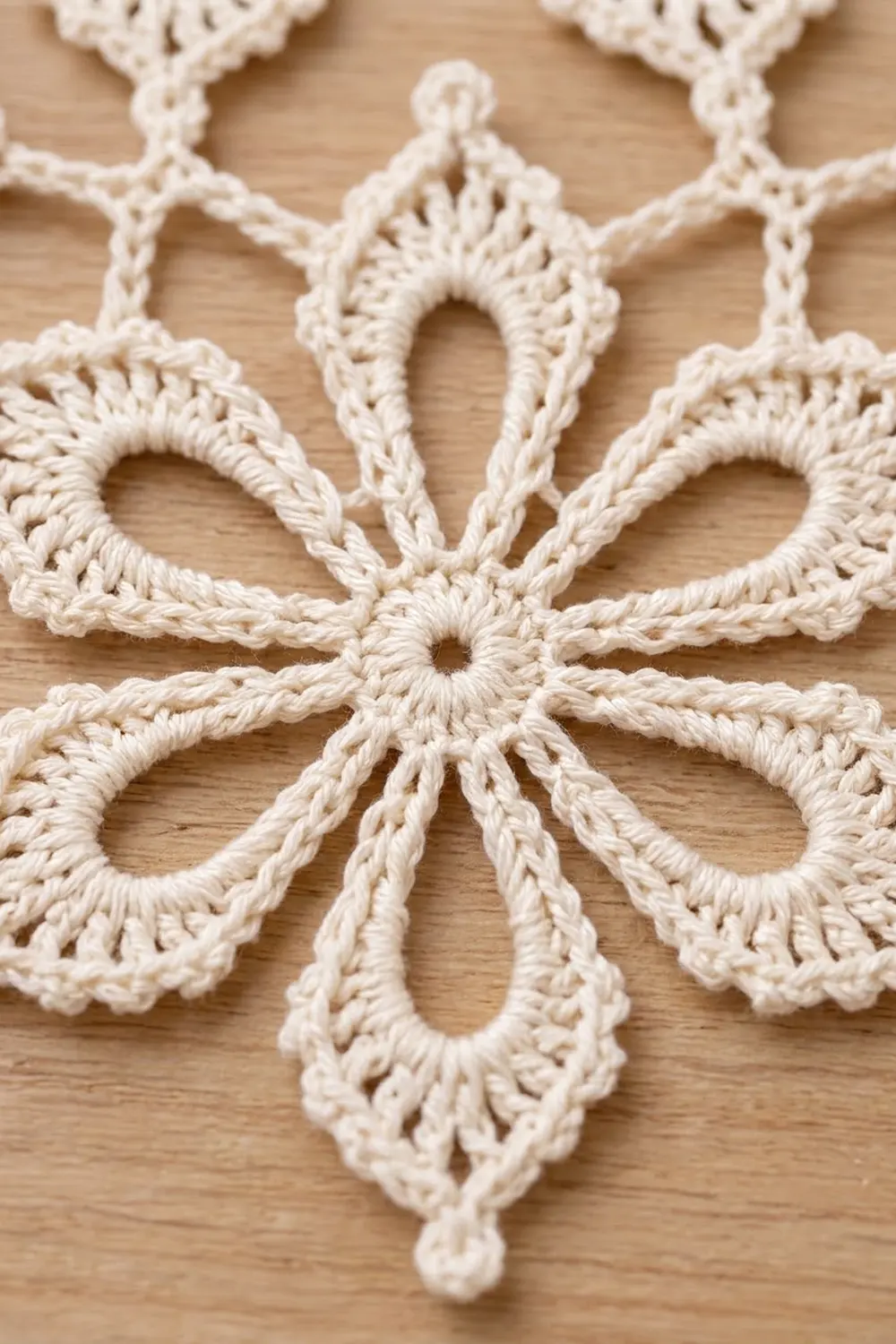 Detailed cream-colored crocheted lace doily with ornate teardrop openwork patterns displayed on light natural wood.