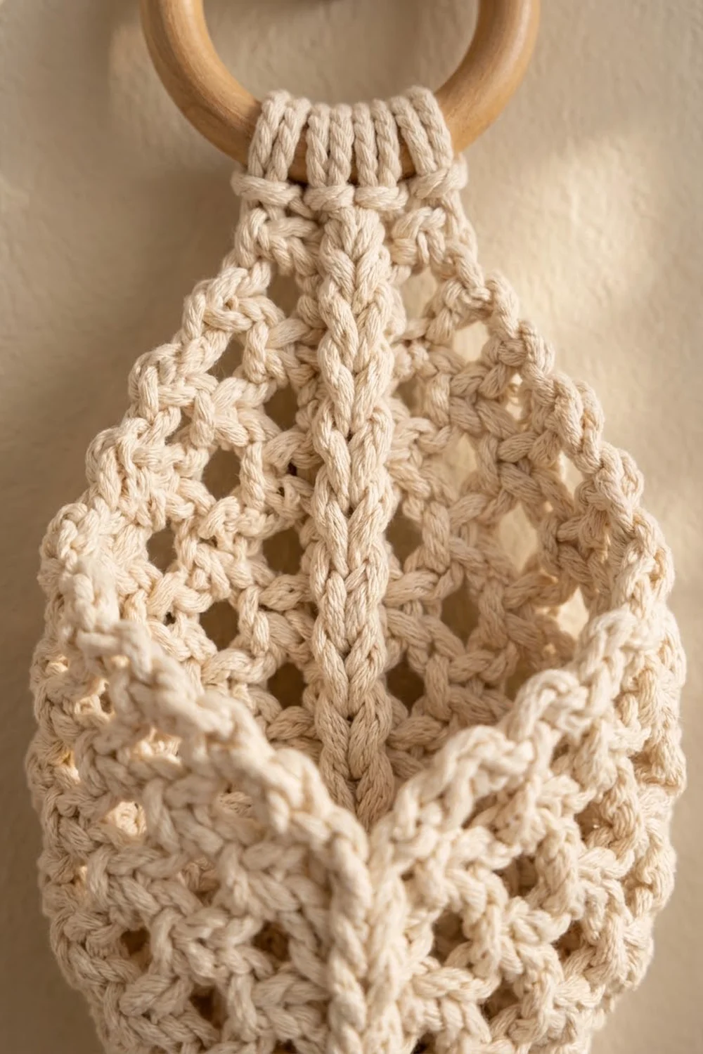 Close-up of cream-colored macramé with intricate knotwork and braided patterns, anchored by a wooden ring.
