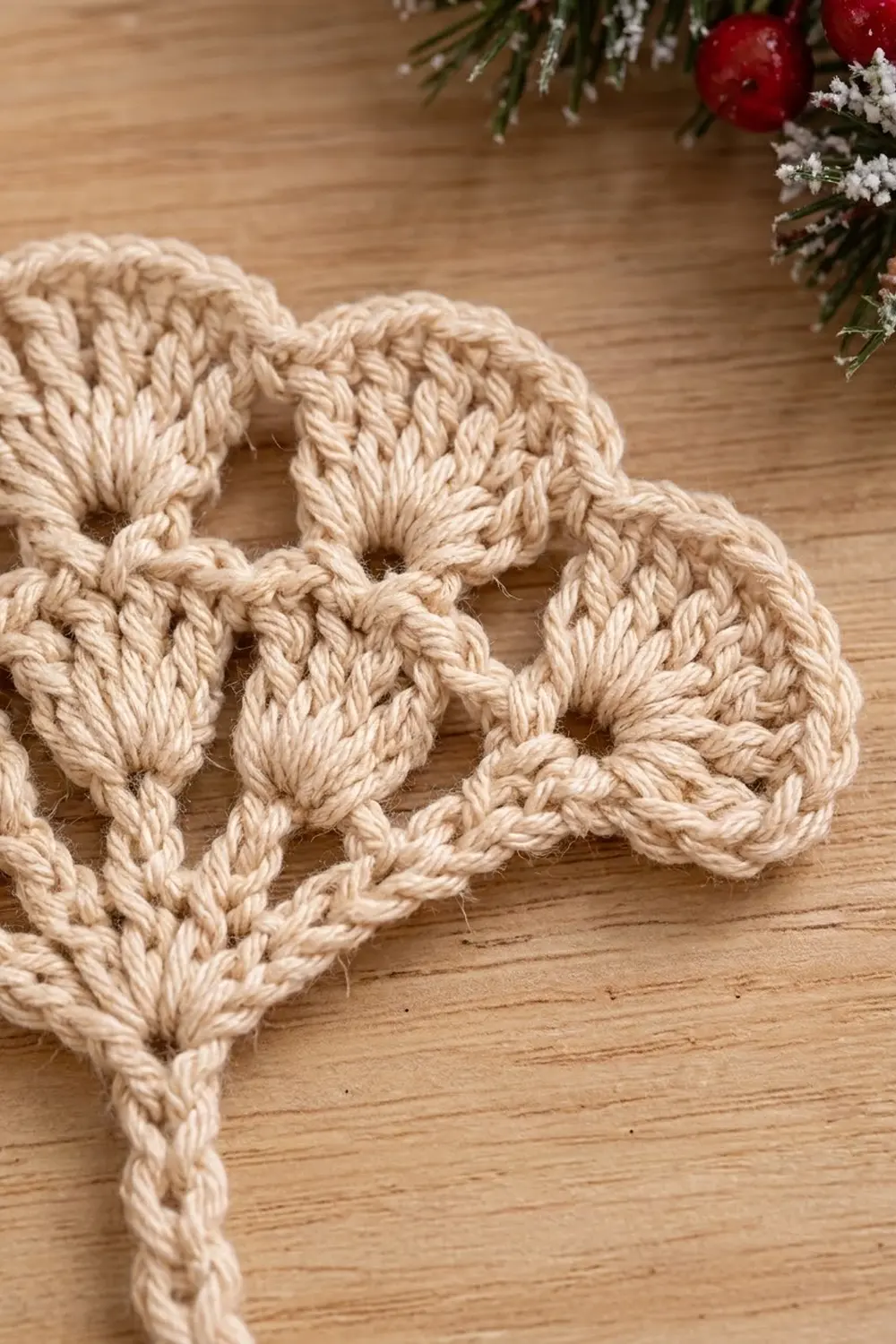 Interlocking cream crocheted chain links on wooden surface with holiday greenery and red ornaments nearby.