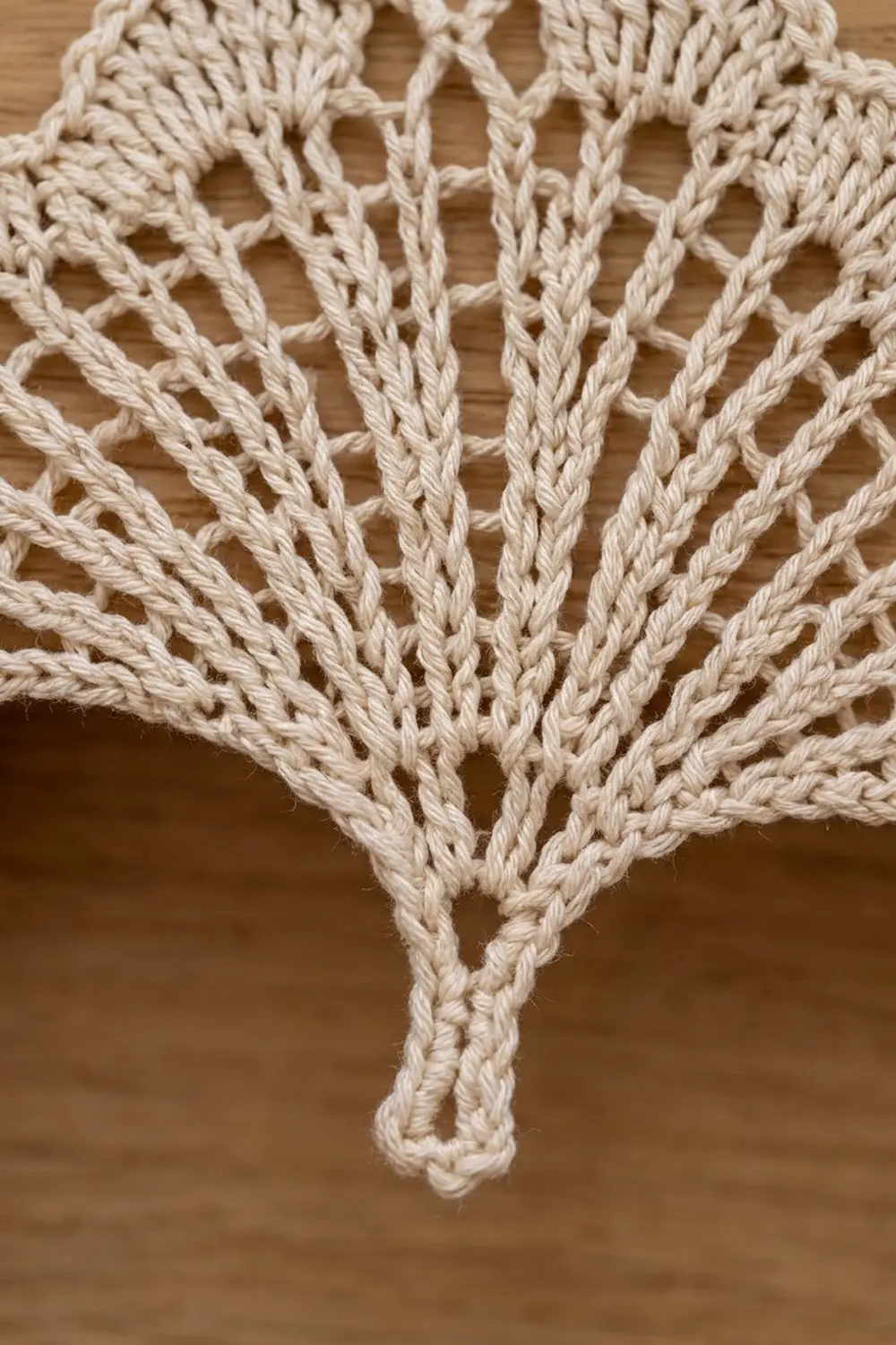 Cream-colored crocheted textile with open lace pattern featuring vertical twisted strands against a soft wooden background.
