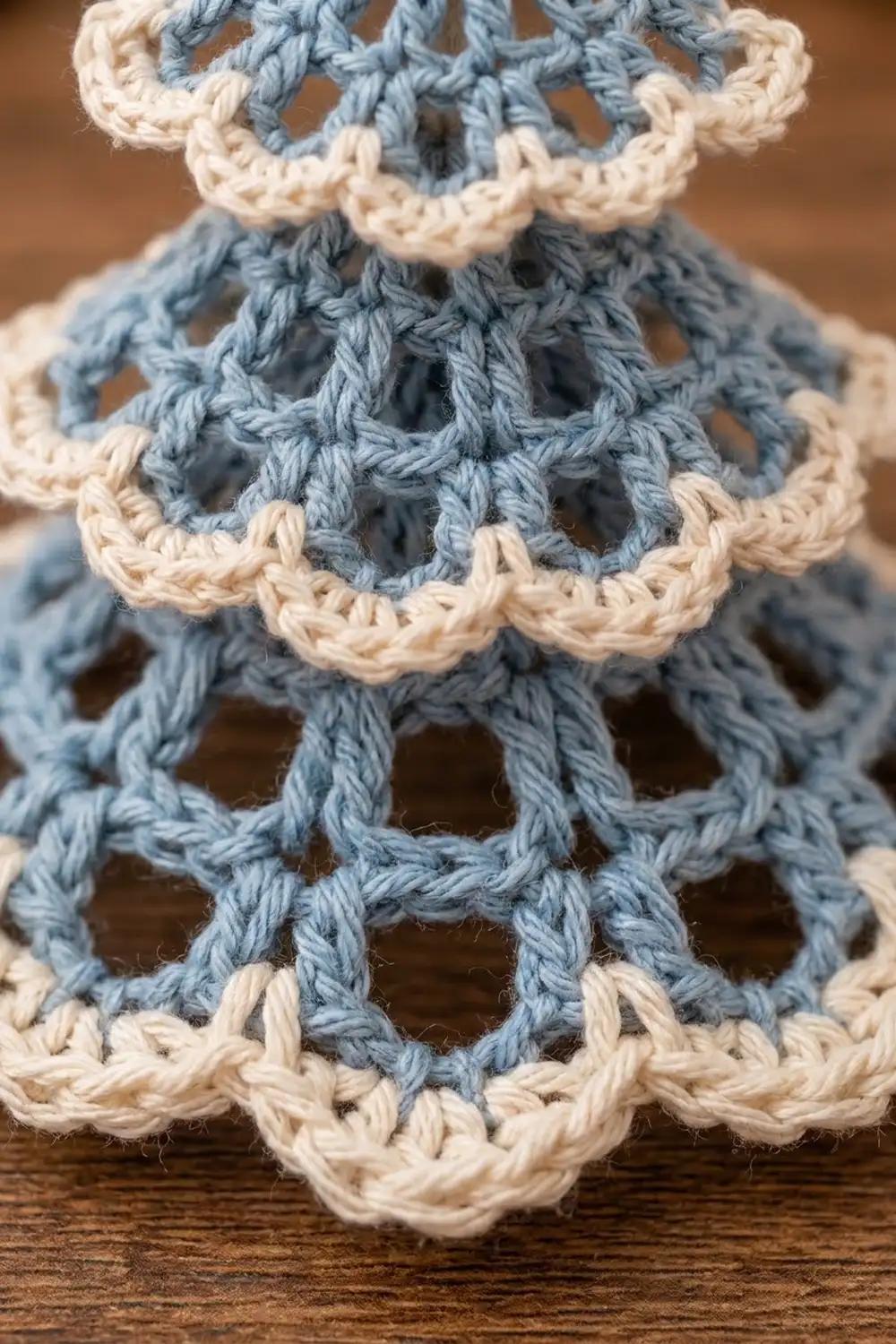 Close-up of a blue and cream crocheted amigurumi bear displaying detailed stitches and openwork pattern against a warm wooden background.