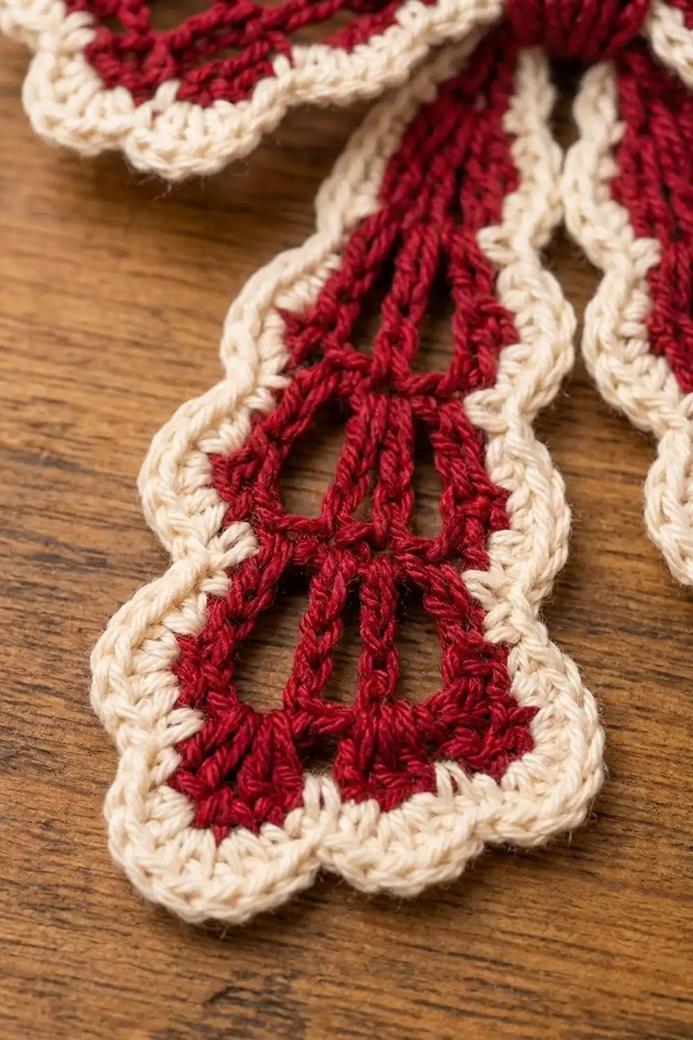 Red and cream crocheted trim with geometric openwork pattern draped across a wooden surface.