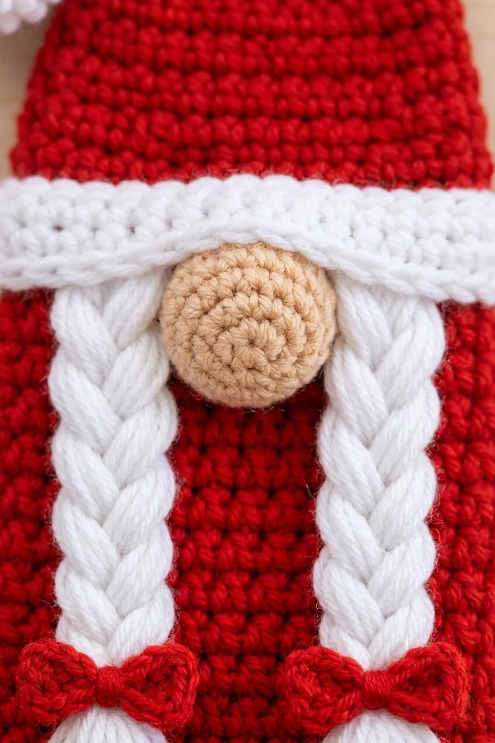 Detail of a red and white crocheted Santa gnome with tan head and braided white beard trim.