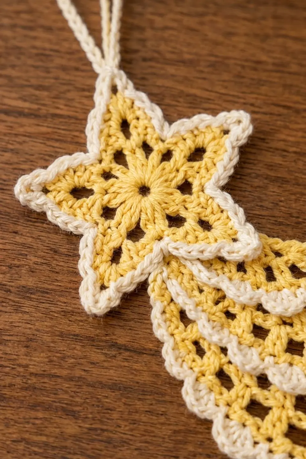A golden-yellow and cream crocheted snowflake with delicate lacework hangs against a warm wooden surface.