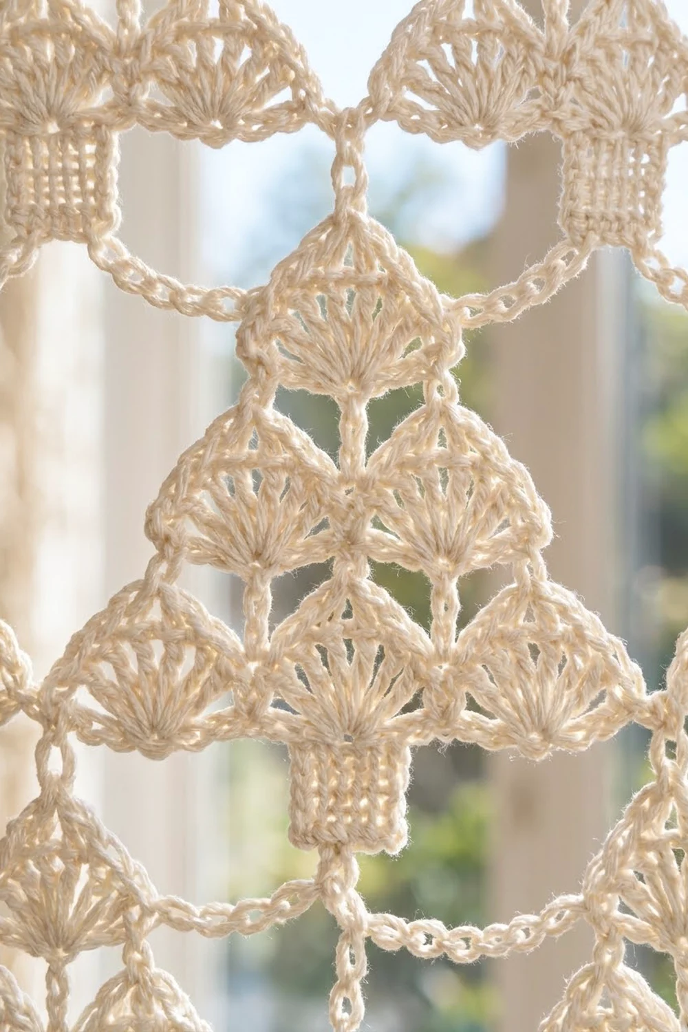 Cream crocheted lace with diamond patterns and spherical embellishments, displayed against softly blurred natural light bokeh.