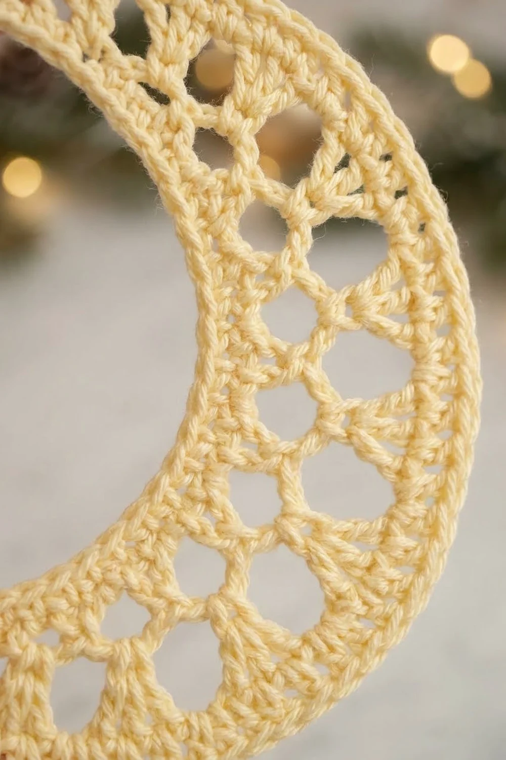 Close-up of cream-colored crocheted lace trim with geometric circular openwork pattern against blurred background.