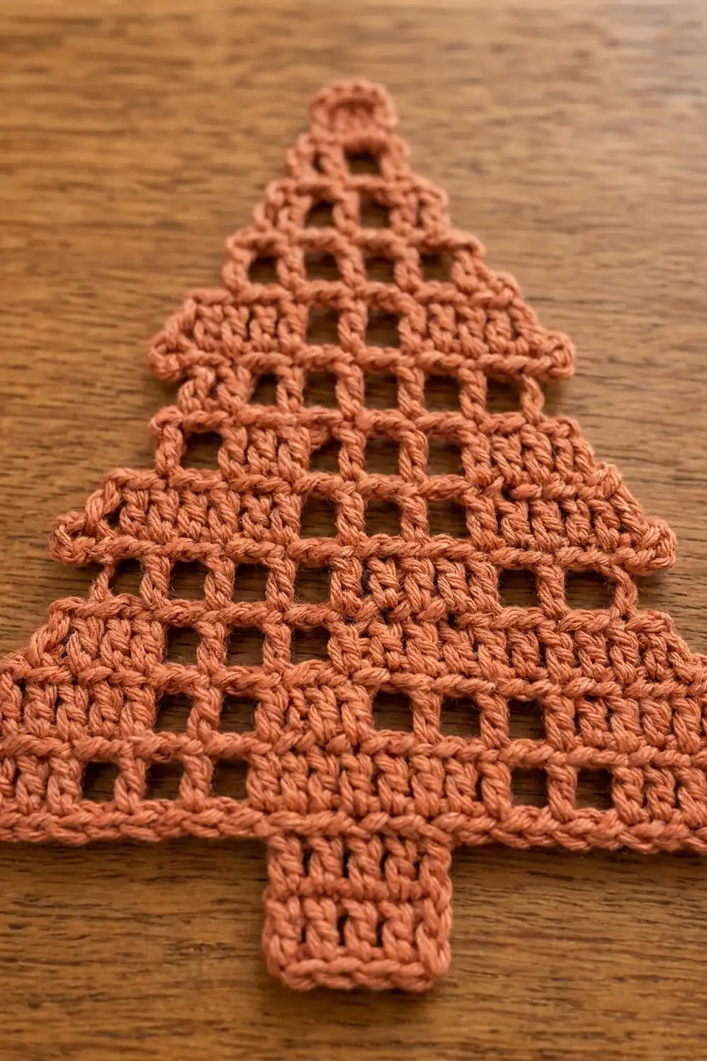 Coral crocheted Christmas tree with open lattice pattern resting on wooden surface.
