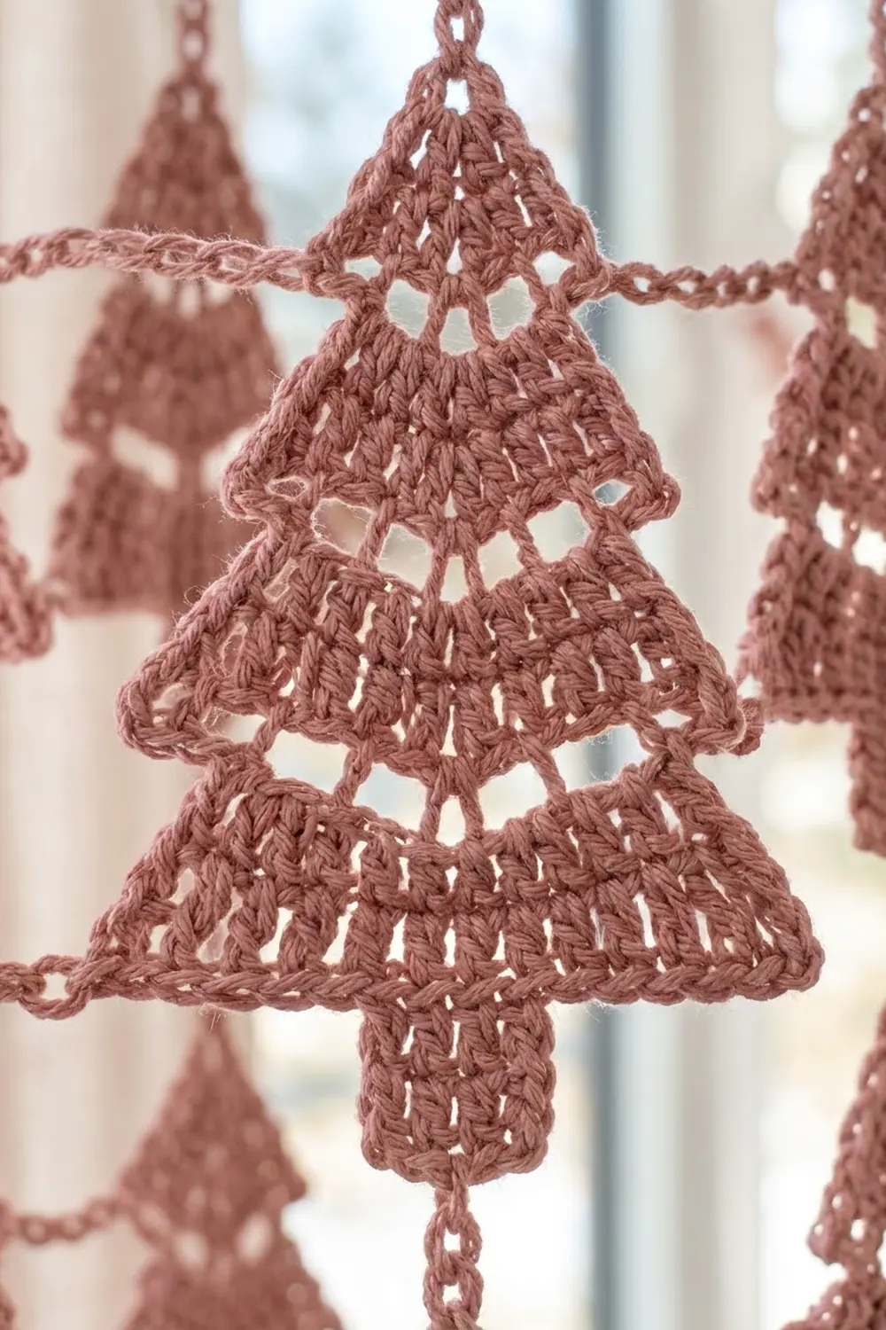 Mauve crocheted tree ornament with delicate openwork pattern hangs among similar decorations in a soft-focus display.