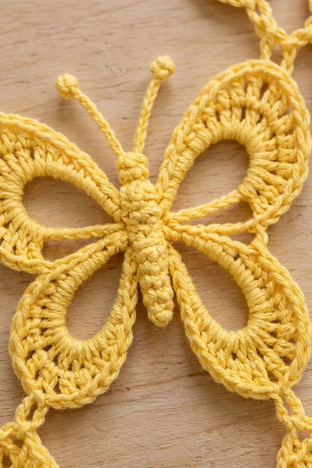 A golden crocheted butterfly with detailed wings and long antennae sits on light wood.