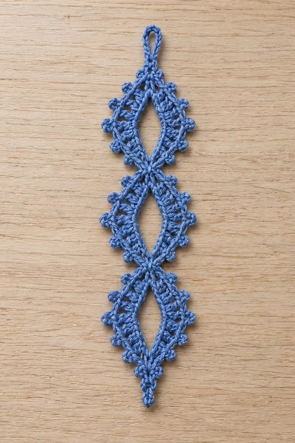 Blue crochet lace ornament with textured bobbles and openwork diamond pattern on light wood.