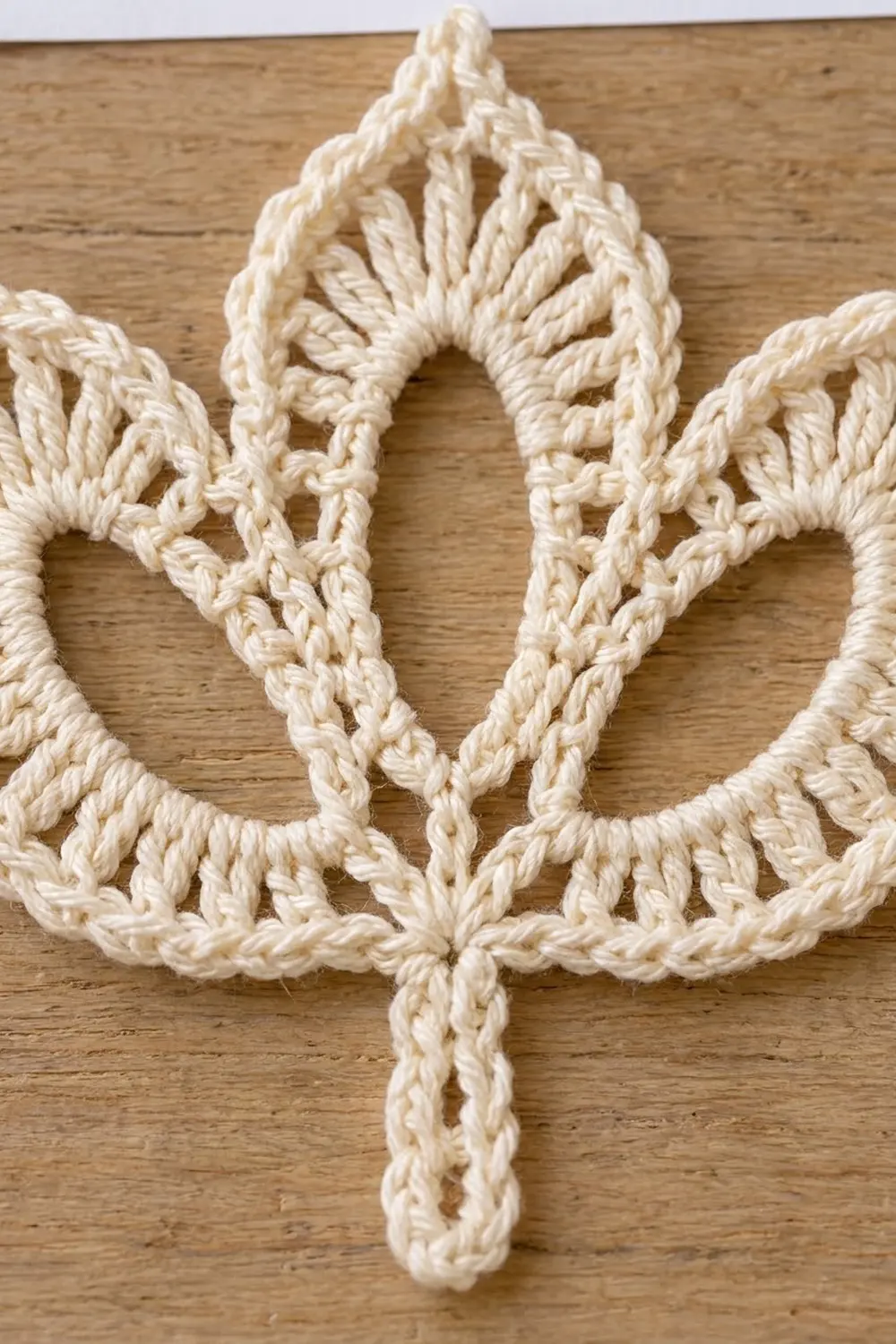 Crocheted cream yarn forming an intricate star shape with geometric lace openwork on a wooden table.