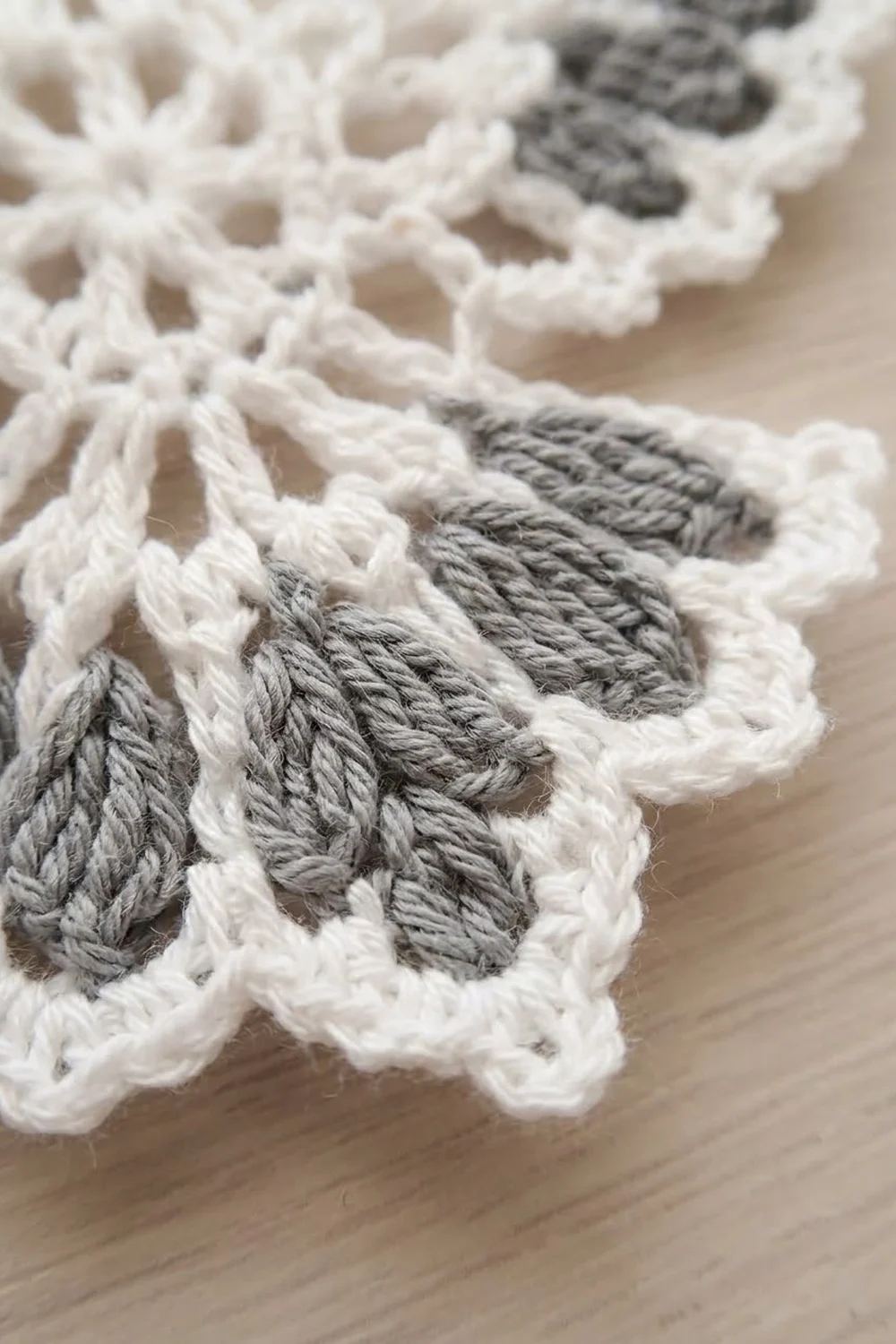 Close-up of crocheted snowflake ornaments with white and gray yarn details on a light wooden surface.